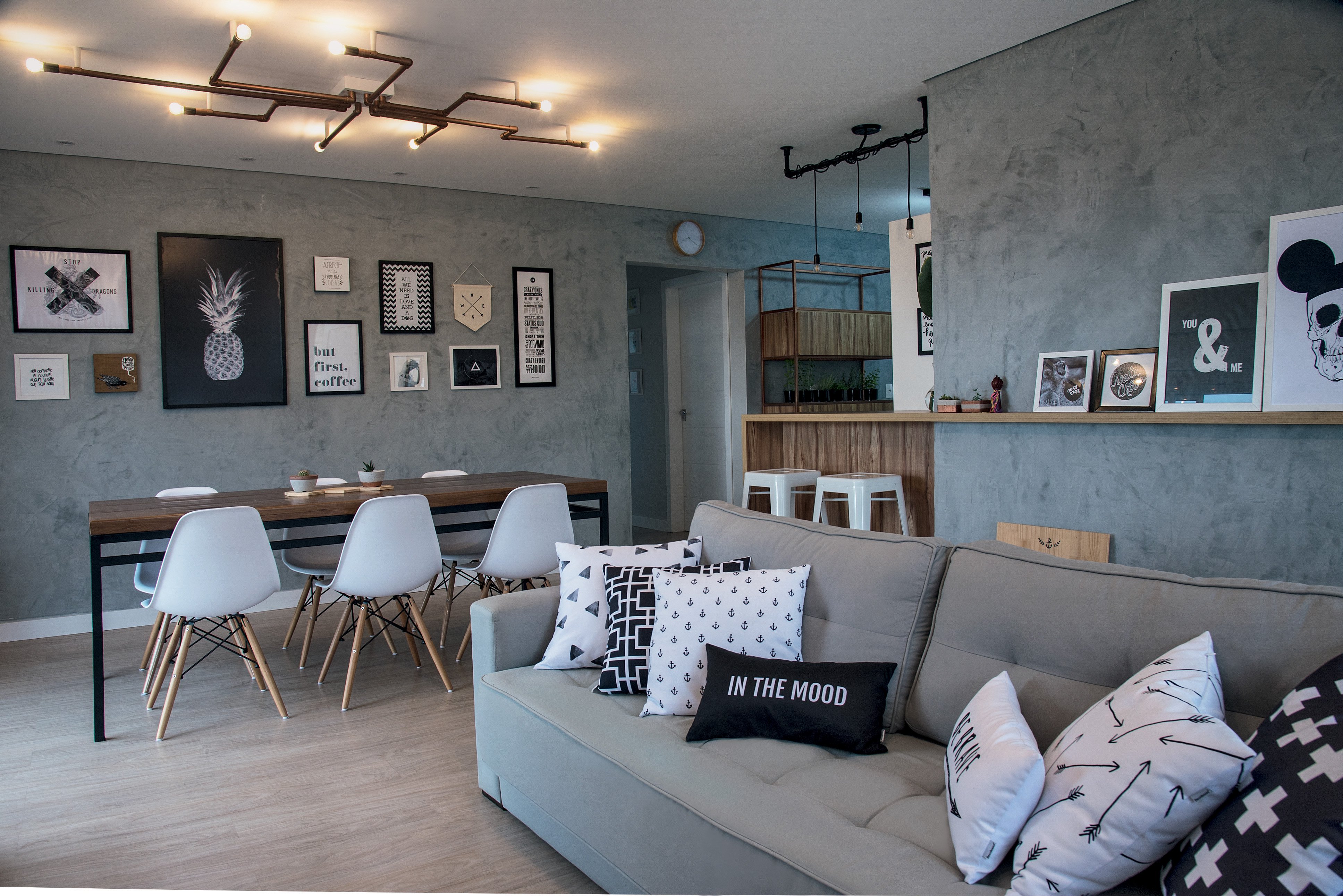 Este apartamento segue à risca o estilo escandinavo em tons neutros, cimento, piso de madeira, mesa com pés de metal, luminárias aparentes e molduras em P&B com grafismos.