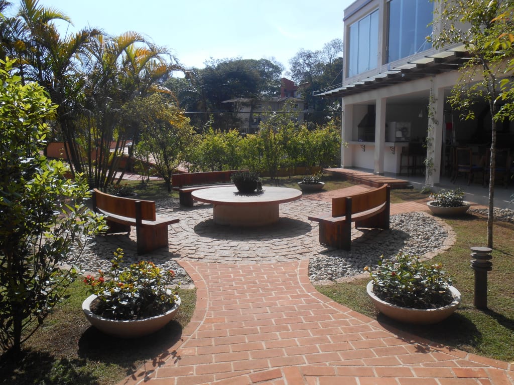 Jardim moderno com bancos e mesa em área circular central no quintal da casa.
